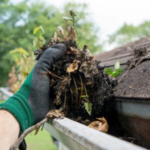 how to prepare your house for winter  - person with glove cleaning debris out of clogged rain gutter